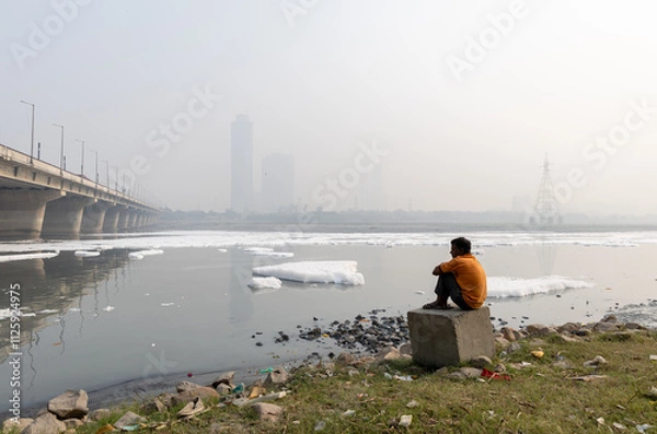 Fototapeta Isolated man looking at Toxic Foam in Contaminated River with Bridge Near Foggy City at morning