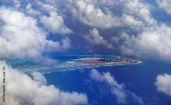 Fototapeta Aerial view from airplane window of Male, Maldives in scattered fluffy clouds layers. High flight of plane over blue sea and island with beach, coral reef. Scenic cloudscape and tropical climate