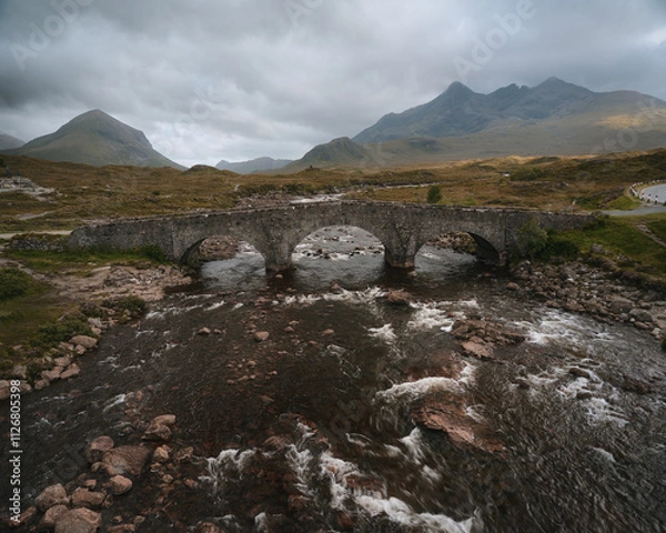 Fototapeta A mountain river and an old stone bridge against a backdrop of mountain peaks. Sligachan Old Bridge, Isle of Skye, Scotland, UK