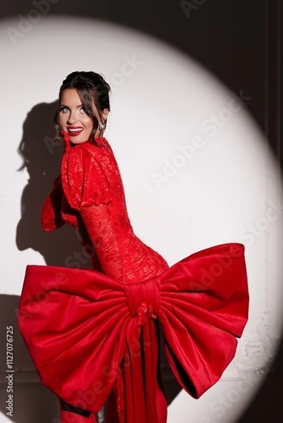 Obraz Stylish brunette in bold red attire and dramatic bow, radiating joy in vivid studio setting