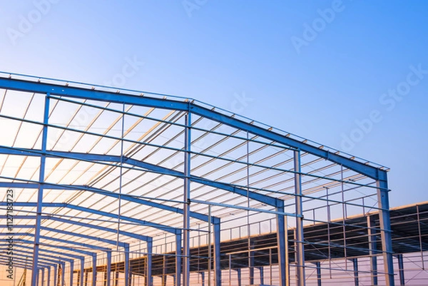 Obraz Factory building framework with metal post and roof beam structure  in construction site against evening sky background, low angle view