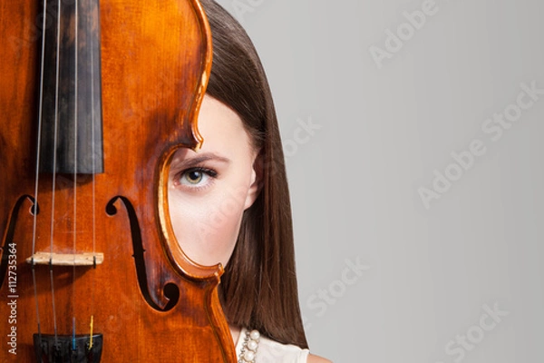 Fototapeta Close-up of beautiful woman looking at camera with one eye near violin