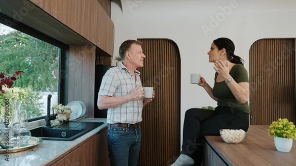 Obraz Lovely old marriage couple happily talking about good event or news in kitchen while holding coffee cup to drink. Cheerful grandfather and grandmother have happy relationship and family. Divergence.