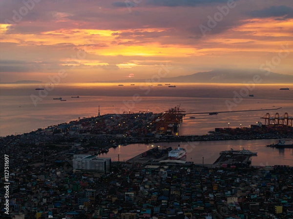 Obraz Manila's lively port area at sunset, featuring cargo ships dotted across the horizon against a dramatic sky with colorful clouds, and city lights twinkling below