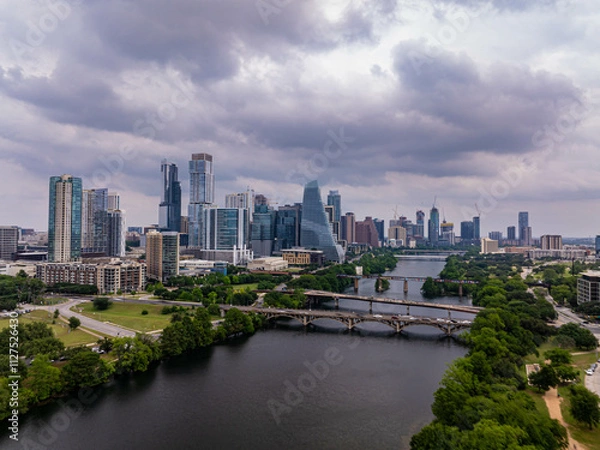 Obraz Aerial view of Austin skyline rising majestically above Colorado River, with a dramatic cloudy sky adding a touch of drama to the urban landscape
