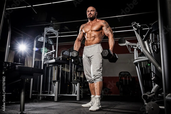 Fototapeta strong and handsome young man doing exercise with dumbbells