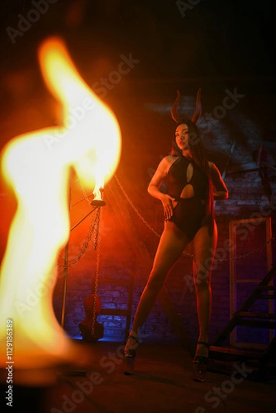 Fototapeta Beautiful asian woman a demon with evil horns posing on a dark background in red lights.