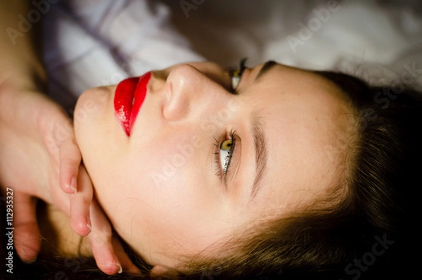 Fototapeta green eyes sensual pinup girl romantic beautiful young woman with big lips having fun touching herself posing relaxing lying on a white bed & looking up at copy space closeup image