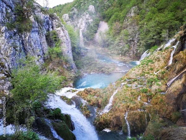 Fototapeta Waterfall in Plitvice lake, Cascading Through Lush Green Forest and Rocky Cliffs