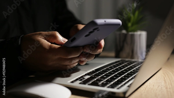 Obraz Programmer using smartphone and laptop working at night on cybersecurity project