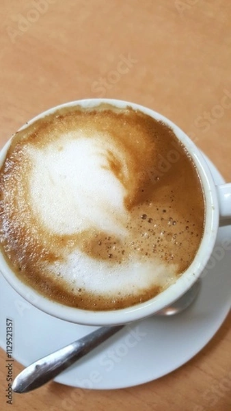 Fototapeta Close up de uma xícara de café com leite, pires branco e colher, sobre mesa marrom.