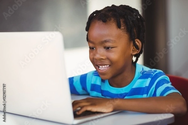Fototapeta Smiling schoolboy using laptop in classroom