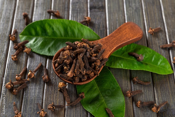 Obraz Dry clove buds in a brown wooden spoon macro. Scoop full of whole organic cloves spice and green leaves over dark wooden background. Spice concept.