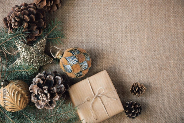 Obraz A gift wrapped in paper is placed on a burlap background, surrounded by Christmas beautiful decorations. Copy space. Vintage style.