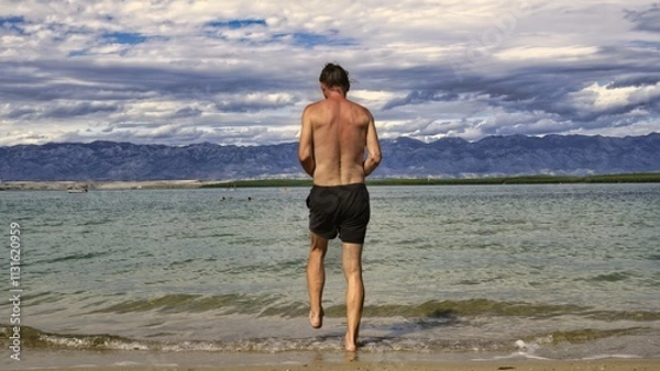 Fototapeta man enters the water 
beautiful mountains in the distance 