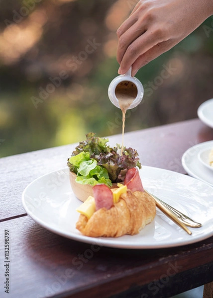 Obraz Delicious ham and cheese croissant served with a fresh side salad. The golden, flaky pastry is filled with melted cheese and savory ham, creating a perfect blend of crisp, creamy, and savory flavors