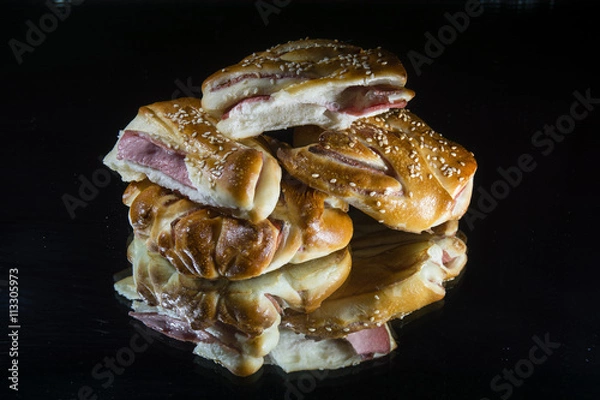 Fototapeta Булочка с запечённой колбасой на тёмном фоне.