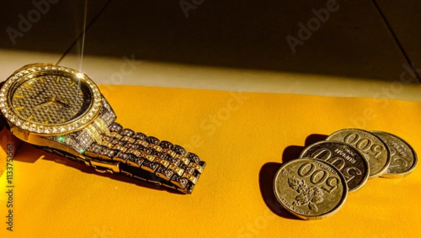 Obraz A shiny luxury watch is placed on a small table, next to coins, with a yellow background.