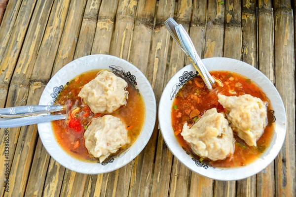 Fototapeta the delicious Two Mie Pentol Bakso or meatball soup in the White bowl with spoon and fork . Two Traditional Food of a Bakso Indonesian .Focus on meatball, Noisy, exposure, similar others
