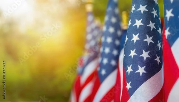 Fototapeta Close-Up View of Vibrant American Flags Waving Outdoors on a Sunny Day with Golden Light and Greenery in the Background. Perfect for Celebrating Patriotic USA Holidays, Memorial Day, or July 4th Event