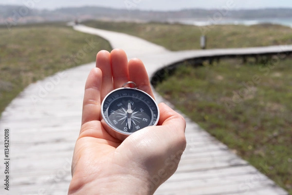 Fototapeta A person holding a compass on a wooden boardwalk. The compass is pointing to the right.
