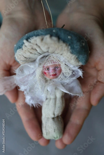 Fototapeta Unique handmade doll figure resembling a mushroom held in hands. A person holds a delicate handmade doll that looks like a mushroom, featuring a painted face and soft textures