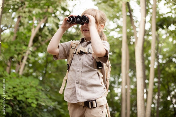 Fototapeta young girl scout, explores  nature with binoculars on camping tr