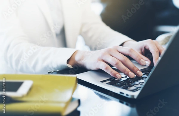 Fototapeta Young woman writing text hands on the open laptop in a cafe on a table with reflection and glare , businesswoman working on computer and smartphone in blue tones