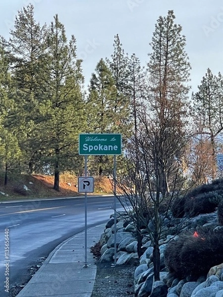 Fototapeta Welcome to Spokane road sign - Pine trees are visible in the background.