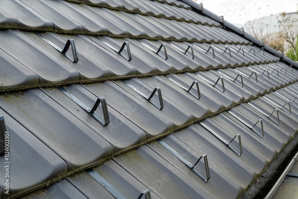 Obraz Snow guards, retainers  or snow hooks on the tile roof. Snow guards to keep snow from sliding off the roof too quickly.
