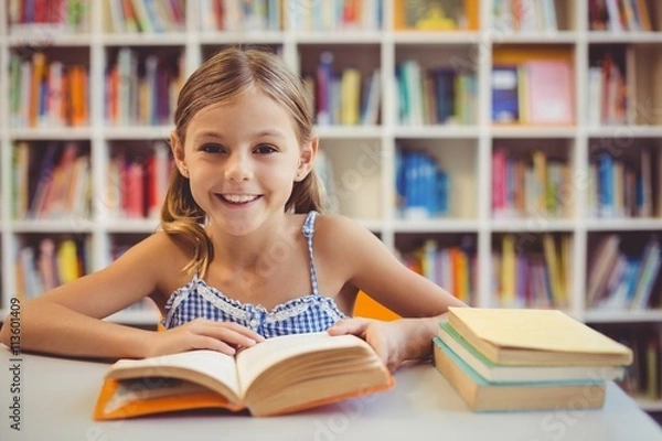 Fototapeta Smiling school girl reading a book in library