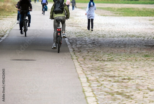 Fototapeta Konzept Nahmobilität im Alltag: Blick auf einen ausgebauten Radweg und Gehweg mit mehreren Radfahrern und Fußgängern – viel Copy Space im Vordergrund