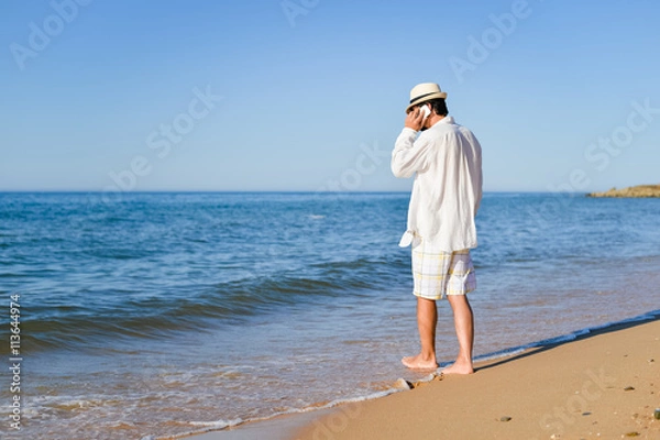 Fototapeta Busy man calling by mobile phone on sandy beach outdoors