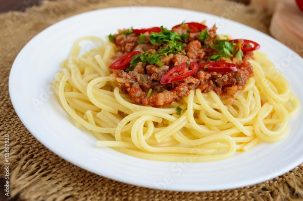 Fototapeta Spaghetti Bolognese with chili on a white plate on a wooden background. Close up