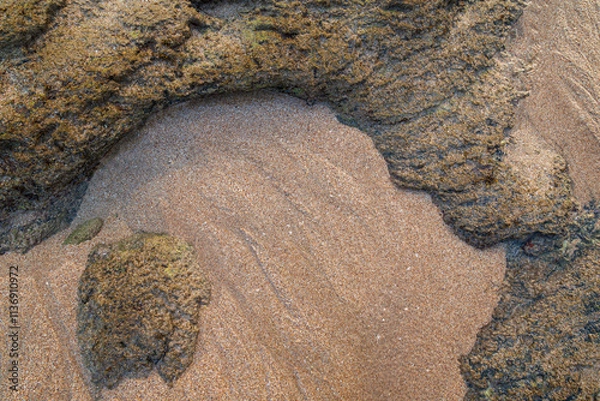 Fototapeta Smooth untouched fine sand and rough sandy rocks on a beach on a sunny day, viewed from above. Abstract textured natural sandy background, top view. Copy space.