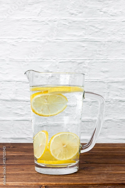 Obraz Water with lemons in jug on wooden table.