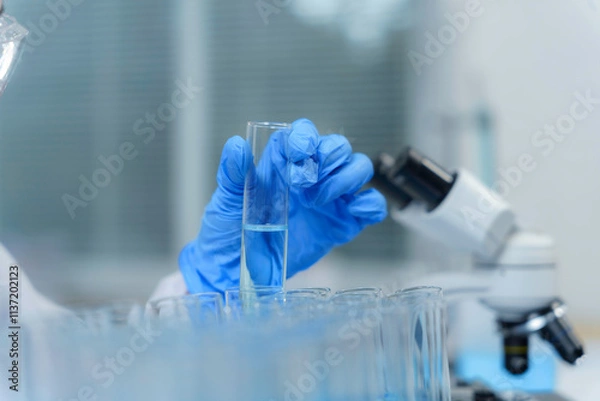 Fototapeta Scientist adding a reagent to a test tube during an experiment in a laboratory with a microscope in the background