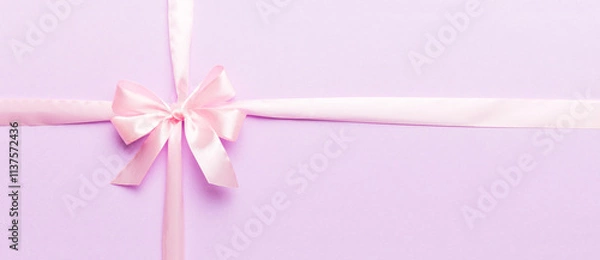 Fototapeta Top view of purple ribbon rolled and pink bow isolated on colored background. Flat lay with copy space