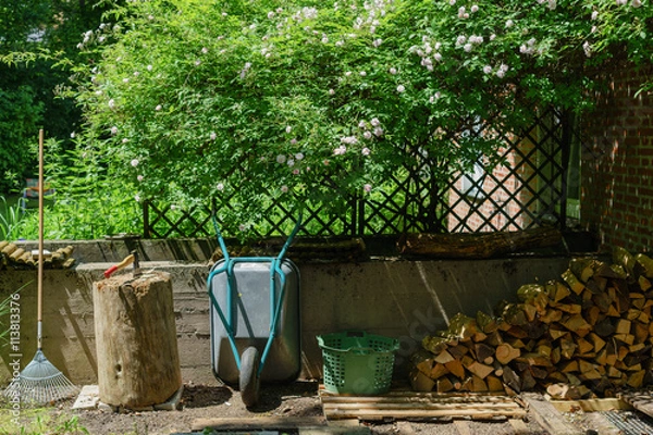 Fototapeta Hackstock mit Beil, Scheite und Stapel Brennholz in der Gartenec