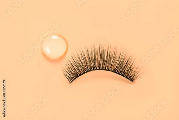 Fototapeta False eyelash and drop of glue on orange background. Women beauty and eyelash extensions.