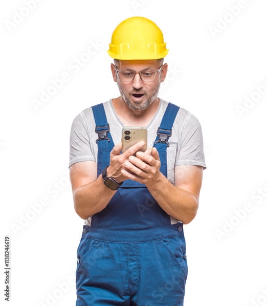 Fototapeta Unexpected message on smart phone. Surprised middle-aged construction worker with phone browsing, isolated on white background. Unbelievable. Craftsman against white wall