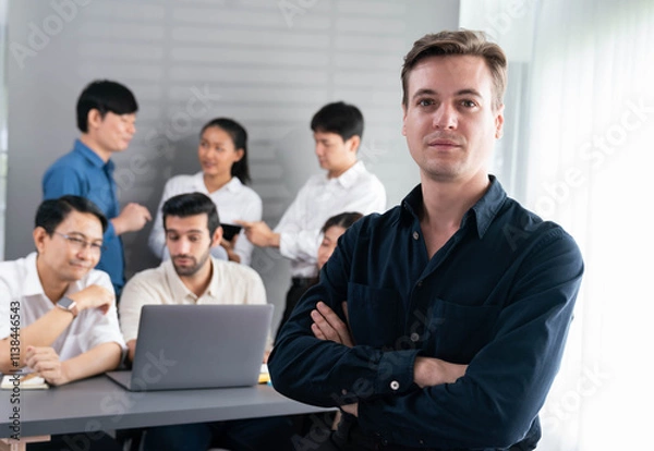 Fototapeta Confidence and happy smiling businessman portrait with background of his colleague and business team working in office. Office worker teamwork and positive workplace concept. Prudent