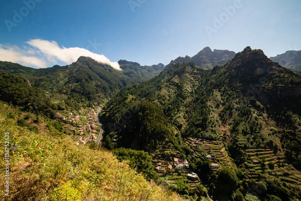 Fototapeta Sunlight cascading over Madeira’s green mountains, highlighting terraced farmland and winding roads through the serene countryside.