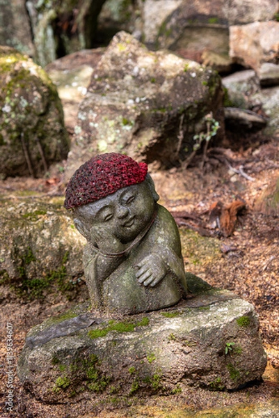 Fototapeta A baby buddha statue wearing a red cap in the forest.
