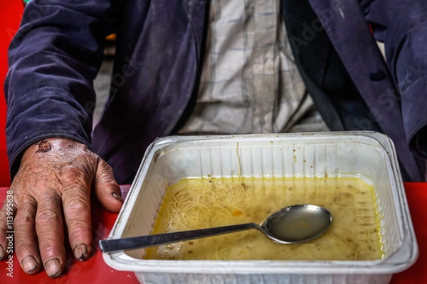 Fototapeta Old and wounded homeless man sitting at the table, with food. 
