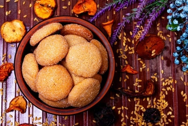 Fototapeta homemade cookies in a clay plate, wheat, dried fruits, herbs and berries on a brown background