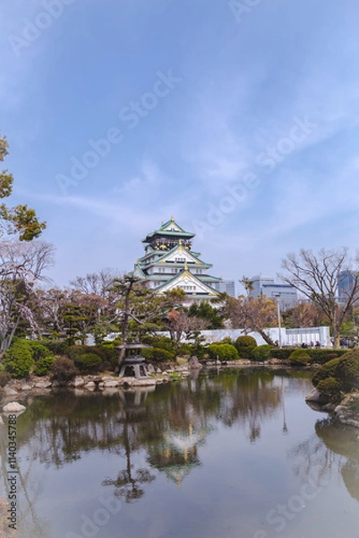 Fototapeta Osaka Castle, A beautiful park with a pond and a large building in the background