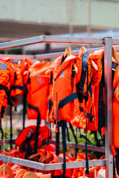 Obraz Multiple Bright Orange Life Jackets Arranged on a Rack for Safety Equipment Display