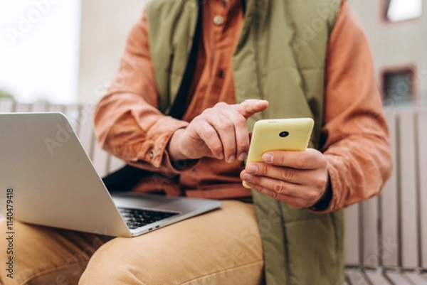 Fototapeta Portrait of man, freelancer wearing casual clothes, holding mobile phone, using laptop, text message