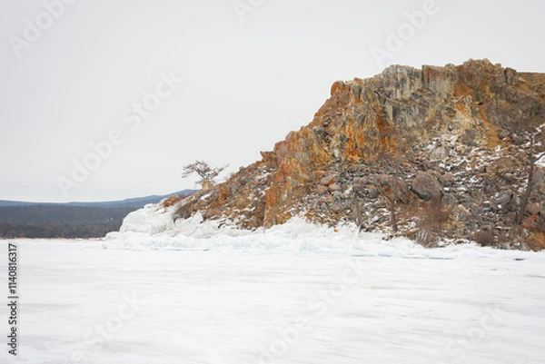 Fototapeta The sky is cloudy and the sun is setting, creating a moody atmosphere. View of Mount Shamanka, Lake Baikal in winter